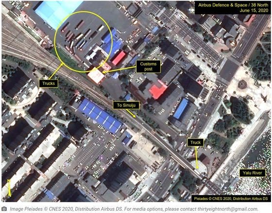 图为商业卫星6月15日拍到的朝中边境地区卫星照片。黄色圆圈内可见正在等待通过边防审查的16辆卡车。【照片来自38 North】