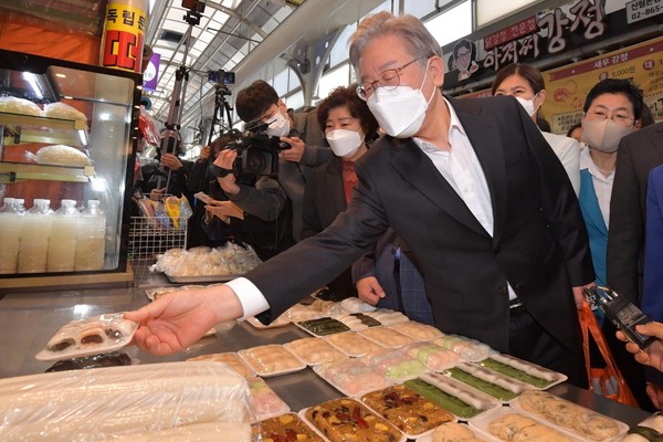 图为共同民主党总统候选人李在明10月27日访问首尔冠岳区信元市场，正在一个商店购买年糕。他在当日的座谈会上表示，“正在考虑制定餐饮店许可限量制度”。【国会摄影记者团】