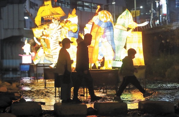 图为23日晚在釜山金井区釜山地铁长箭站附近的温泉川举行的2021金井文化庆典"梦幻之光旅行"展，市民们正在观看展示的50多件流灯。亮灯时间是17点至22点。