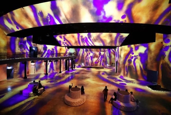 继济州“光之地堡”之后，第二个光之系列沉浸式展厅“光之剧场”将于27日在首尔广津区开馆。开馆展是“古斯塔夫·克里姆特， Gold in Motion”，这是对被称为“20世纪金色画家”古斯塔夫·克里姆特作品的全新诠释。“光之剧场”是将1963年开馆的“华克山庄剧场”翻新打造的空间，规模宏大，拥有投影机和服务器、扬声器、影音自动化系统、3D音响等最新技术，可展现3000个以上高清授权图像。图为25日，在首尔广津区华克山庄酒店举行的沉浸式媒体艺术展示场“光之剧场”中前来参加展前活动的人们正在欣赏作品。【照片来源：NEWS1】 【照片来源：韩联社】