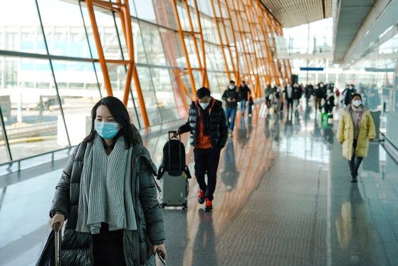 图为上月28日中国北京首都机场，佩戴口罩的旅客拿着行李入境。【照片来源：欧新社】