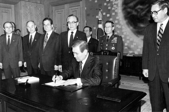图为1992年2月17日，卢泰愚总统在郑元植总理(右一)等人的注视下签署《韩朝基本协议》和《韩半岛无核化共同宣言》的场景。【中央图片库】