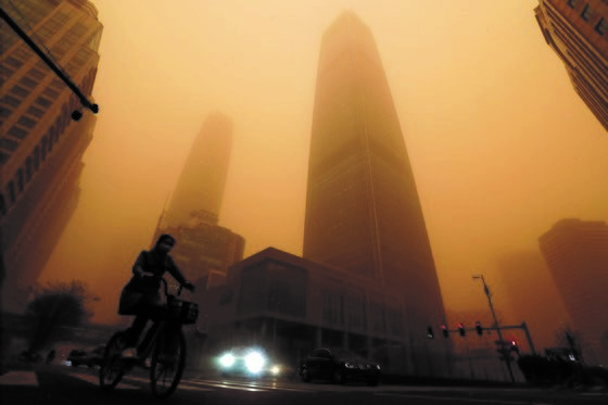 图为3月15日，在沙尘暴覆盖下的北京，某市民正骑着自行车走在北京街头。【照片来源：美联社】