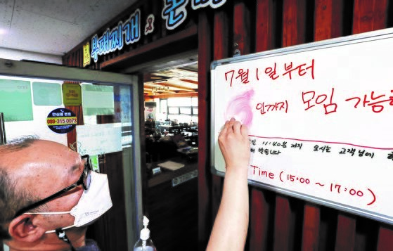 图为6月30日韩国政府突然宣布推迟一周实施放宽保持距离规定的新版防疫措施后，首尔某餐饮店的老板无奈将写好的“7月1日起允许6人聚会”招牌上的数字擦掉。【照片来源：韩联社】