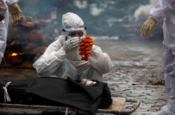 图为今年7月，印度一名新冠肺炎死者的亲戚正身穿防护服、手持花束蹲在死者遗体前呜咽。【照片来源：美联社=韩联社】