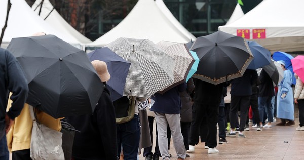 在首尔中区首尔广场设立的新型冠状病毒肺炎(COVID-19)临时筛查所，市民们打着伞站在雨中等待接受检查。【照片来源：NEWS1】
